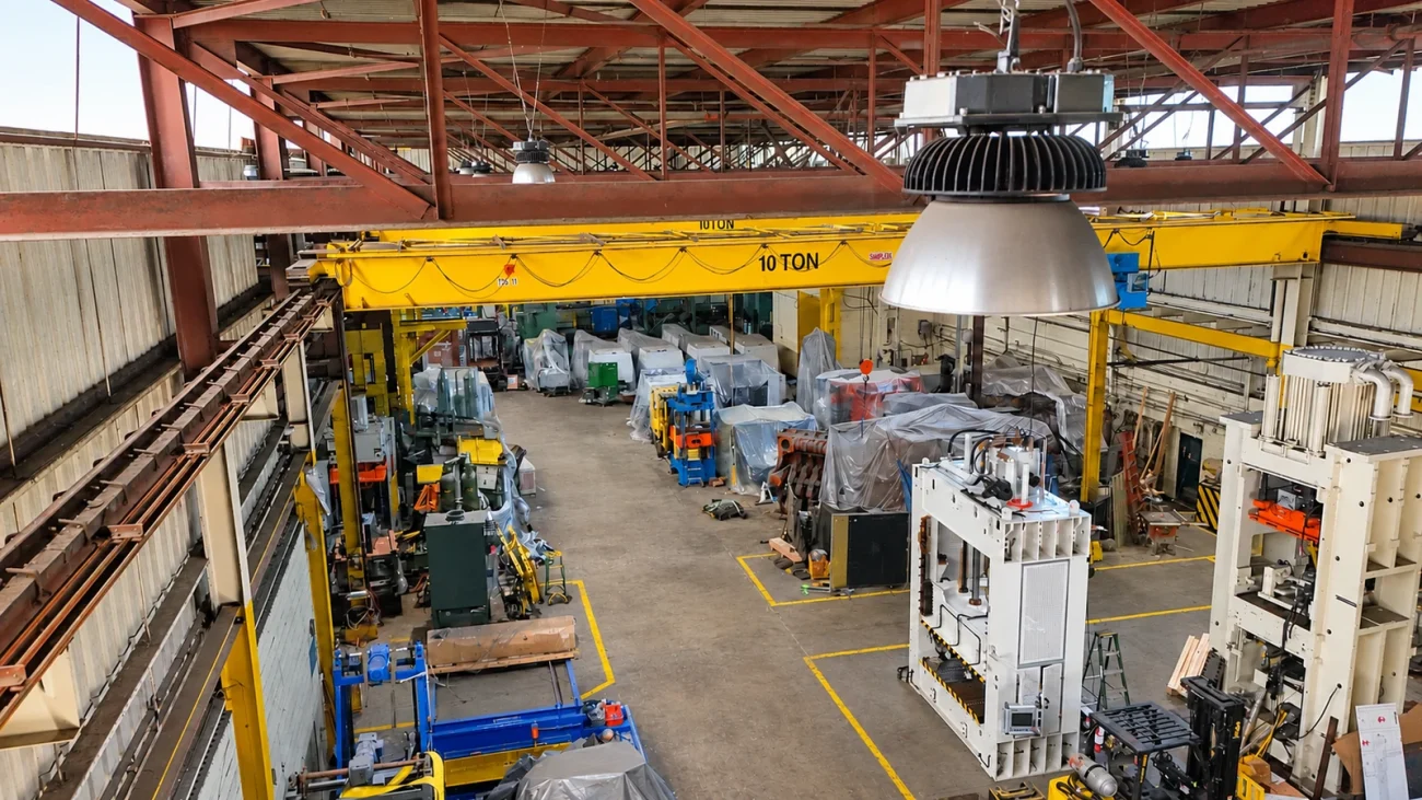 Stored industrial machines beneath yellow overhead cranes in the shared Cambridge warehouse.